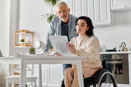 Un homme en fauteuil roulant et une femme examinant un document dans un cadre de cuisine confortable à la maison.