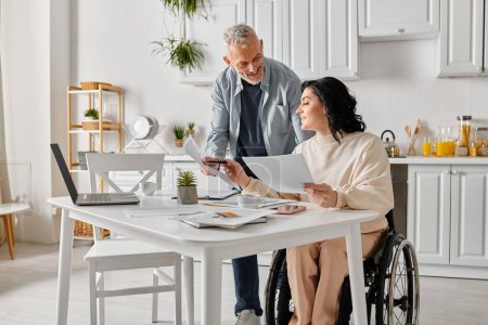 Téléchargez les photos : Un homme et une femme en fauteuil roulant inspectent de près un morceau de papier dans leur cuisine à la maison. - en image libre de droit