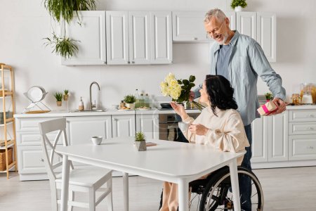hombre cariñosamente da un ramo de flores a su esposa en una silla de ruedas en su cocina en casa.