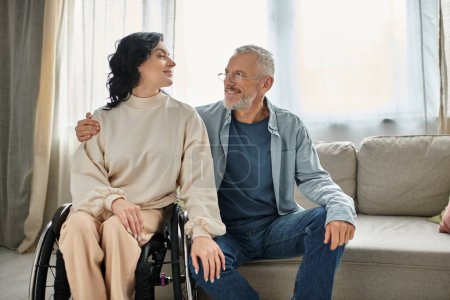 A disabled woman in a wheelchair engages in conversation with a man in the living room.