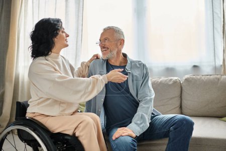 Eine Frau im Rollstuhl im Gespräch mit einem Mann, beide in einem herzlichen Gespräch in gemütlicher Wohnzimmeratmosphäre.