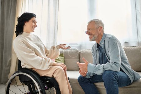 Un homme discute avec une femme handicapée en fauteuil roulant dans un cadre confortable salon.