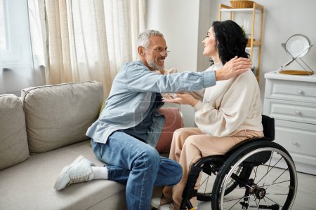 A disabled woman in a wheelchair is hugging her husband in a caring and supportive manner in their living room.