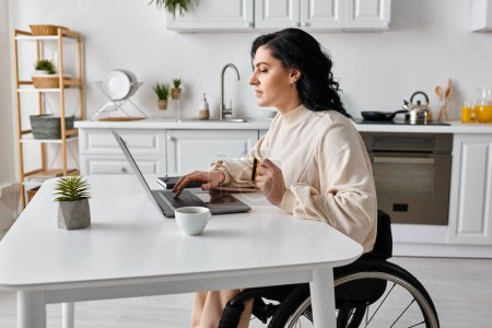 Téléchargez les photos : Femme handicapée dans un fauteuil roulant travaillant sur un ordinateur portable dans sa cuisine. - en image libre de droit