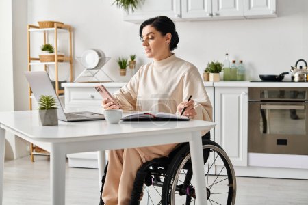 Une femme handicapée dans un fauteuil roulant travaille sur son ordinateur portable à la maison dans la cuisine, montrant la productivité et l'indépendance.