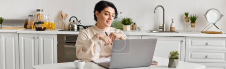 femme s'assoit à sa table de cuisine, concentrée sur son écran d'ordinateur portable tout en travaillant à distance.