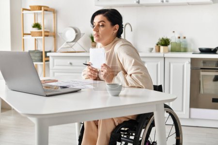 Une femme handicapée dans un fauteuil roulant travaillant à distance sur son ordinateur portable depuis sa cuisine.