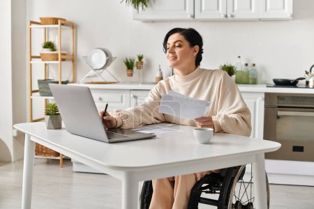 Una mujer discapacitada en una silla de ruedas trabajando remotamente desde su cocina, usando una computadora portátil en una mesa.