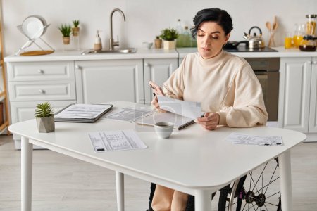 Une femme handicapée en fauteuil roulant s'assoit à une table de cuisine avec des papiers et une tasse de café, concentrée sur des tâches à distance.