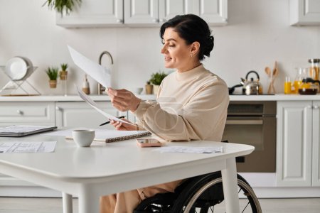A disabled woman in a wheelchair sits in her kitchen, holding a piece of paper while working remotely.