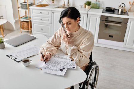 Una mujer discapacitada en silla de ruedas lee un papel mientras trabaja de forma remota desde su cocina.
