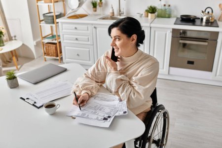 A disabled woman in a wheelchair is working remotely from her kitchen, seated at a table.