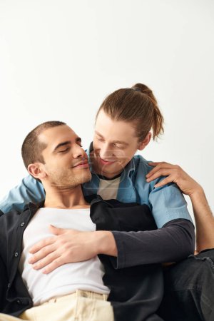 A man sits on top of another man on a couch in a loving and intimate moment.