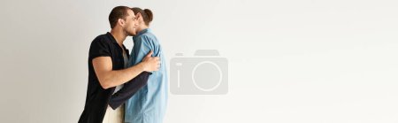 A man hugs his partner tightly under a blue blanket.