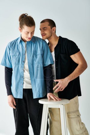 Téléchargez les photos : Deux hommes se tiennent près d'un tabouret, partageant un moment de proximité. - en image libre de droit