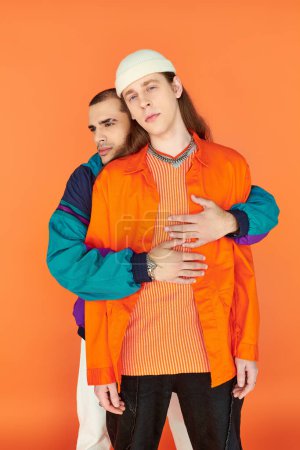 Foto de Una pareja gay amorosa se encuentra lado a lado contra un atrevido telón de fondo naranja. - Imagen libre de derechos