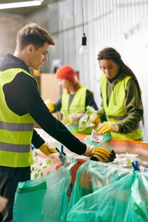 Foto de Young volunteers in gloves and safety vests, standing around a table filled with bags, sorting trash together. - Imagen libre de derechos