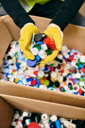 Photo for Volunteer in yellow gloves carefully holding a bunch of colorful bottle caps - Royalty Free Image