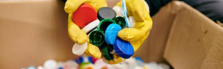 Photo for A young volunteer in yellow gloves holding a bunch of colorful bottle caps while sorting waste - Royalty Free Image