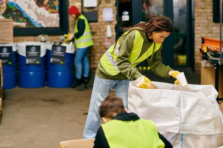 A young woman in a green jacket leads volunteers sorting trash together in safety vests.