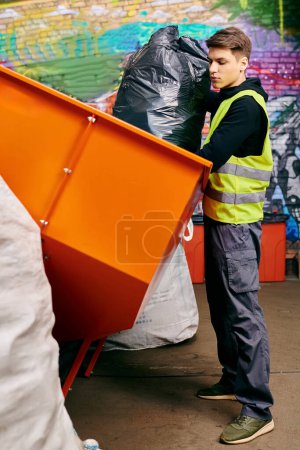 Young volunteer in gloves and safety vest stands next to dumpster, sorting trash in front of a wall.