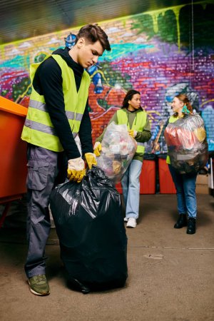Foto de Young volunteers in safety vests and gloves sorting trash for a cleaner environment. - Imagen libre de derechos