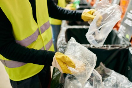 Foto de A person in a yellow vest and yellow gloves joins young volunteers in sorting trash as part of an eco-conscious effort. - Imagen libre de derechos