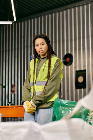 A young volunteer in a yellow vest sorts waste in a warehouse, embodying eco-conscious practices.