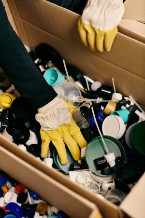 A young volunteer in gloves and a safety vest, sorting through a box filled with a wide variety of items.