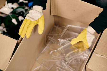 Photo for A young volunteer in yellow gloves and safety vest sorts waste by holding a plastic. - Royalty Free Image