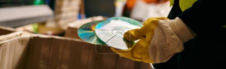 Photo for Young volunteer in gloves and safety vest sorting waste, holding compact discs. Eco-conscious action. - Royalty Free Image