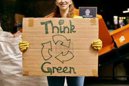 A young volunteer in gloves and safety vest holds a sign that says Think Green while sorting waste, promoting eco-consciousness.