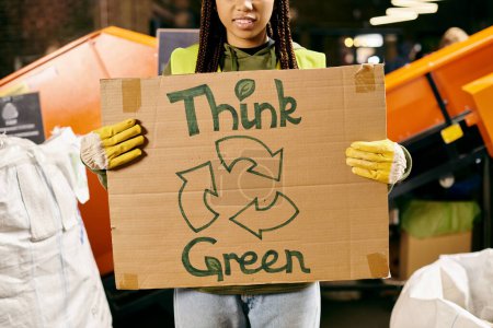 A young volunteer in gloves and safety vest holds a sign saying think green, promoting environmental awareness through action.