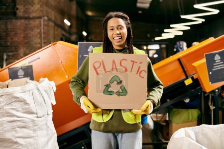 Photo for Young volunteer in safety gear sorting waste, holding a sign that says plastic. - Royalty Free Image