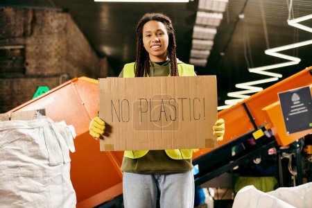 A young volunteer in gloves and safety vest stands proudly, holding a sign that says no plastic to promote environmental awareness.