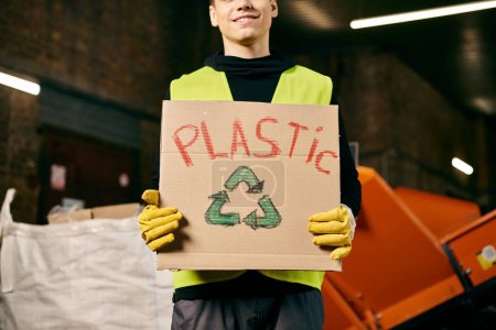 A young volunteer in gloves and safety vest sorts waste, holding a cardboard sign that reads plastic.