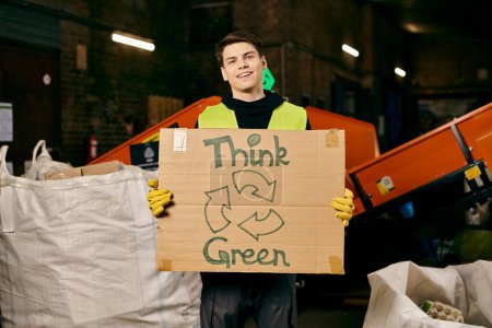 A young volunteer in gloves and safety vest holds a sign that reads think green while sorting waste.