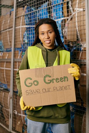 A woman in gloves and safety vest holds a sign urging to go green and save our planet.