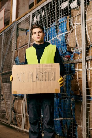 Téléchargez les photos : A young volunteer in gloves and safety vest sorts waste, passionately displaying a no plastic sign. - en image libre de droit