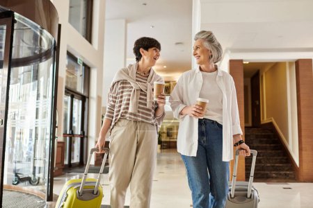 Photo for Senior lesbian couple, one holding luggage, the other holding hands, ready for adventure. - Royalty Free Image