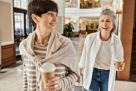 Zwei Frauen genießen einen Spaziergang durch ein Einkaufszentrum, während sie Kaffeetassen in der Hand halten.