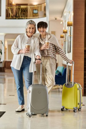 Una pareja lesbiana mayor camina por un pasillo con equipaje.