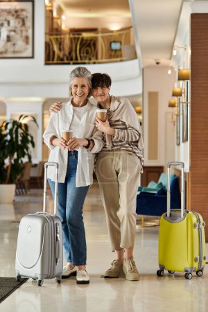 Senior lesbian couple, a loving senior lesbian couple, stand in a hotel lobby with luggage.