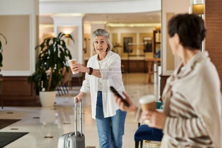 Senior lesbian couple walks through hotel lobby with luggage.