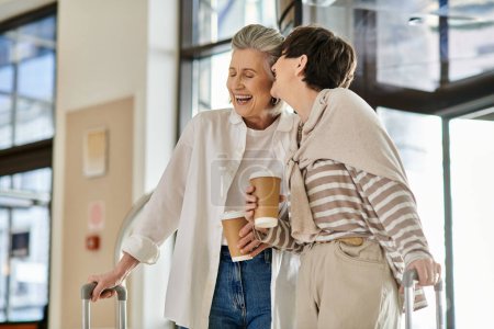 Two senior lesbian women holding luggage and sipping coffee.