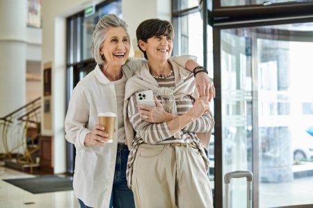 Deux lesbiennes âgées se tiennent devant un hôtel, rayonnant d'élégance et d'amour.