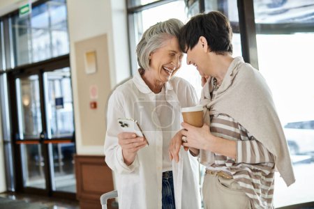 Two loving senior lesbian women standing in a hotel, embracing each other tenderly.