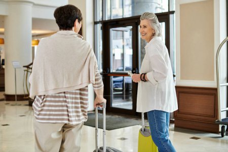 Senior lesbian couple walk hand in hand through a bustling airport.