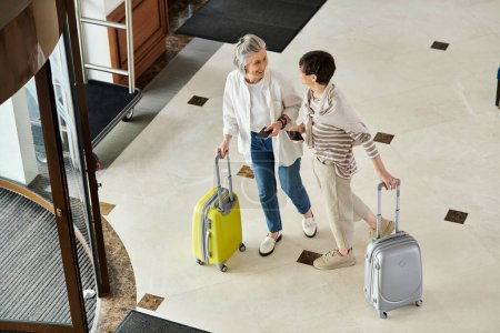 Liebevolles älteres lesbisches Paar steht mit Gepäck in einem Hotel.