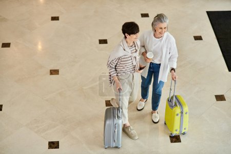 Senior lesbian couple standing with luggage, ready for their journey.